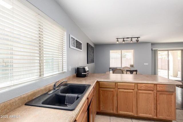 kitchen with light tile patterned floors, a peninsula, a sink, light countertops, and rail lighting