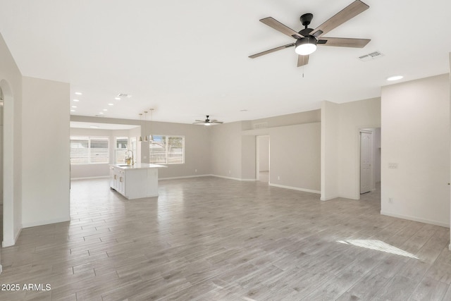 unfurnished living room with sink, ceiling fan, and light wood-type flooring