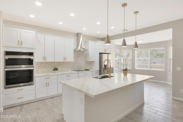 kitchen featuring white cabinetry, wall chimney range hood, hanging light fixtures, and a center island with sink