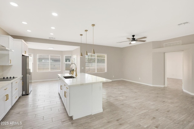 kitchen featuring sink, stainless steel refrigerator, an island with sink, pendant lighting, and white cabinets