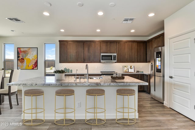 kitchen with a center island with sink, sink, light stone countertops, and stainless steel appliances