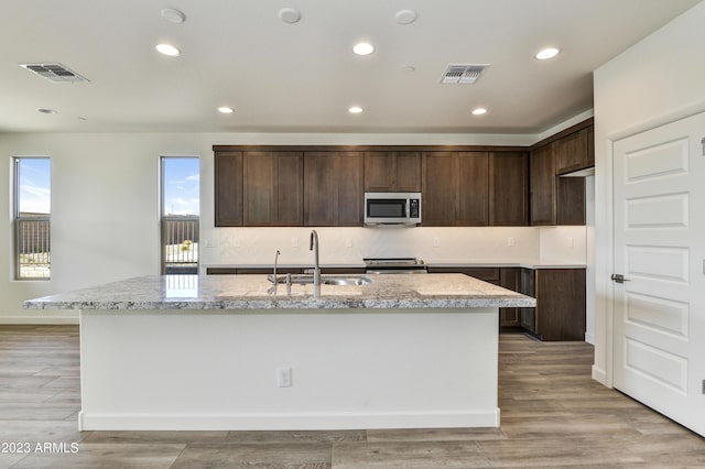 kitchen with light stone counters, sink, stainless steel appliances, and an island with sink