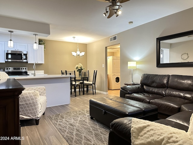 living room featuring stacked washing maching and dryer, ceiling fan with notable chandelier, and light hardwood / wood-style floors