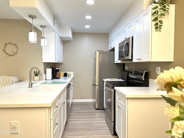 kitchen featuring sink, light hardwood / wood-style flooring, appliances with stainless steel finishes, white cabinetry, and hanging light fixtures