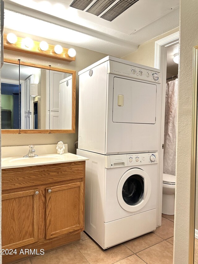 washroom with light tile patterned flooring, stacked washing maching and dryer, and sink