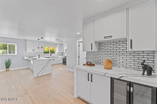 kitchen with white cabinetry, light stone countertops, decorative backsplash, and light hardwood / wood-style floors