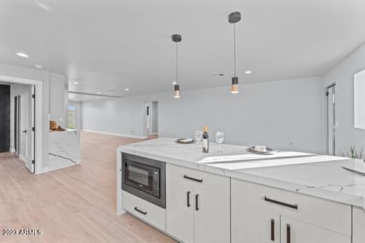 kitchen with decorative light fixtures, light stone counters, black microwave, light wood-type flooring, and white cabinets