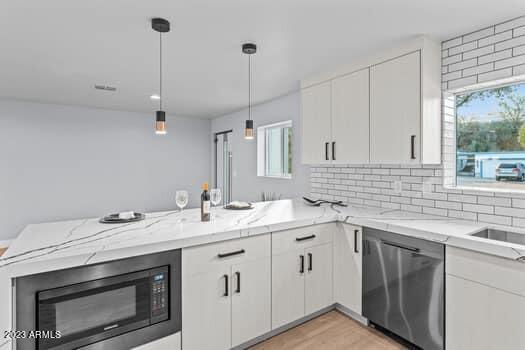 kitchen featuring black microwave, decorative backsplash, kitchen peninsula, and stainless steel dishwasher