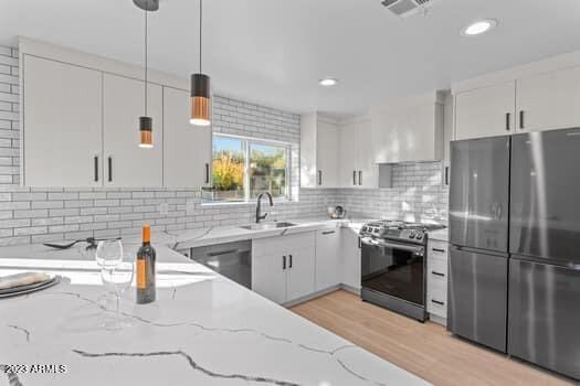 kitchen featuring appliances with stainless steel finishes, light stone counters, white cabinetry, and sink