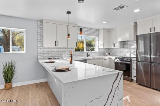 kitchen with white cabinets, appliances with stainless steel finishes, light stone counters, light hardwood / wood-style floors, and kitchen peninsula