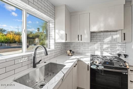 kitchen with sink, tasteful backsplash, gas stove, and white cabinets