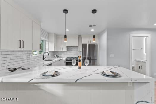 kitchen featuring stainless steel fridge, decorative light fixtures, range, sink, and white cabinets