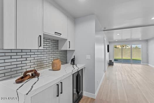 kitchen with wine cooler, light hardwood / wood-style flooring, decorative backsplash, white cabinetry, and light stone counters