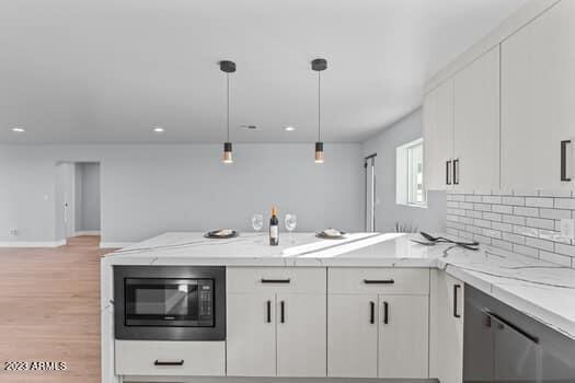 kitchen featuring black microwave, hanging light fixtures, light wood-type flooring, and light stone countertops