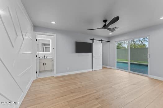 unfurnished bedroom with a barn door, ceiling fan, ensuite bathroom, and light hardwood / wood-style floors