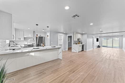 kitchen featuring tasteful backsplash, stainless steel appliances, hanging light fixtures, white cabinets, and light hardwood / wood-style floors