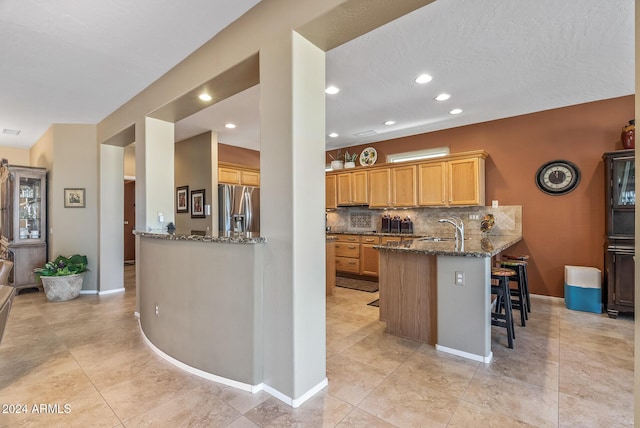 kitchen with sink, stainless steel refrigerator with ice dispenser, decorative backsplash, stone countertops, and kitchen peninsula