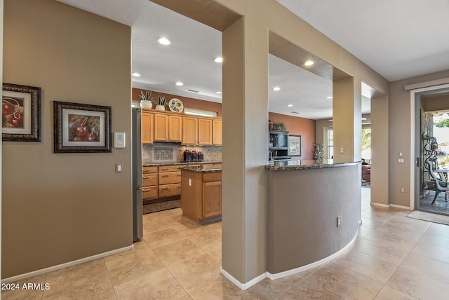 kitchen featuring backsplash, kitchen peninsula, dark stone countertops, and light tile patterned floors