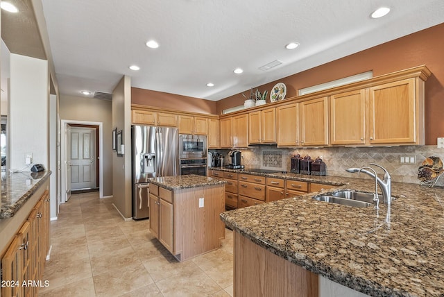 kitchen featuring a center island, sink, stainless steel appliances, backsplash, and dark stone counters