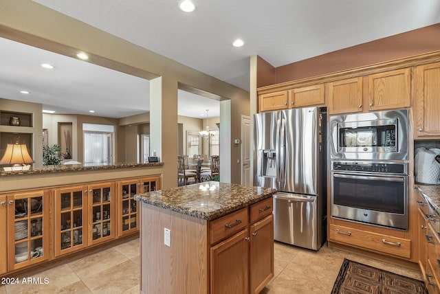 kitchen featuring a center island, dark stone countertops, appliances with stainless steel finishes, light tile patterned flooring, and a chandelier