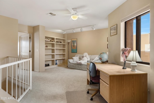 carpeted office featuring visible vents, built in shelves, rail lighting, and a ceiling fan