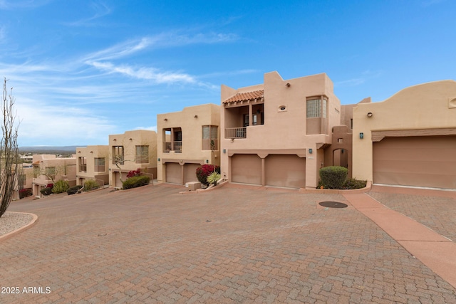 southwest-style home featuring stucco siding, decorative driveway, a residential view, a garage, and a balcony