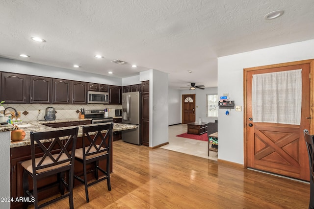 kitchen with stainless steel appliances, light stone counters, a textured ceiling, dark brown cabinets, and light hardwood / wood-style flooring