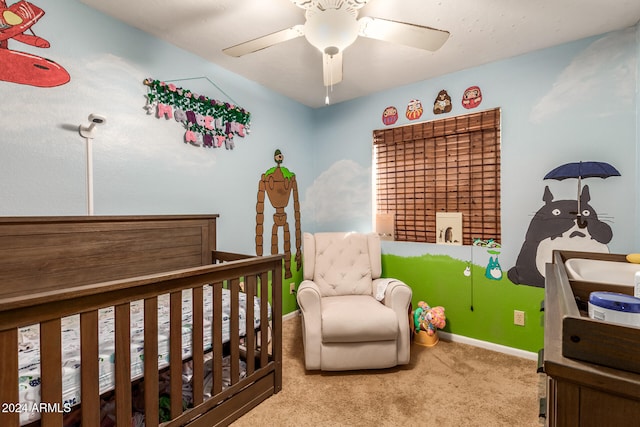 carpeted bedroom with a crib and ceiling fan