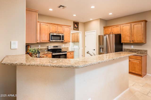 kitchen with sink, light stone countertops, independent washer and dryer, kitchen peninsula, and stainless steel appliances