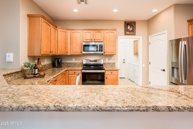 kitchen with washer and dryer, light stone countertops, kitchen peninsula, and stainless steel appliances