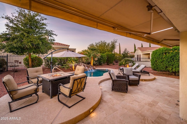 patio terrace at dusk with pool water feature, a fenced in pool, and a fire pit