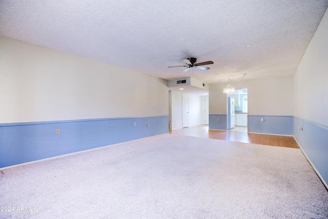 spare room featuring carpet floors, ceiling fan with notable chandelier, and a textured ceiling