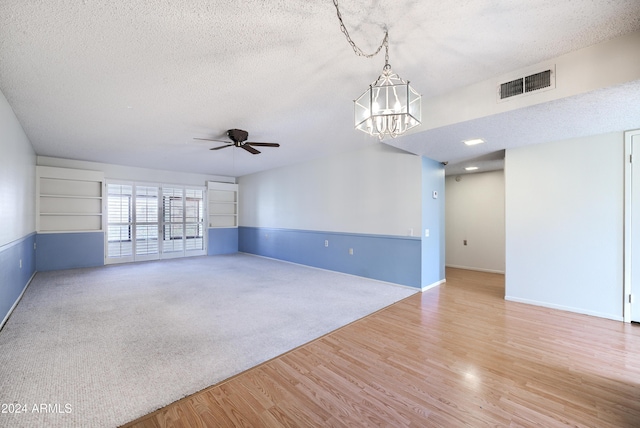 empty room with ceiling fan with notable chandelier, a textured ceiling, and light hardwood / wood-style flooring