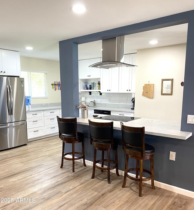 kitchen featuring a breakfast bar area, light wood finished floors, freestanding refrigerator, and island range hood