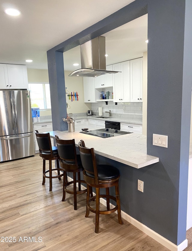 kitchen featuring a kitchen breakfast bar, white cabinets, freestanding refrigerator, tasteful backsplash, and island exhaust hood