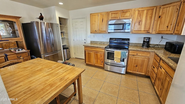 kitchen with stainless steel appliances, light tile patterned floors, and light stone counters