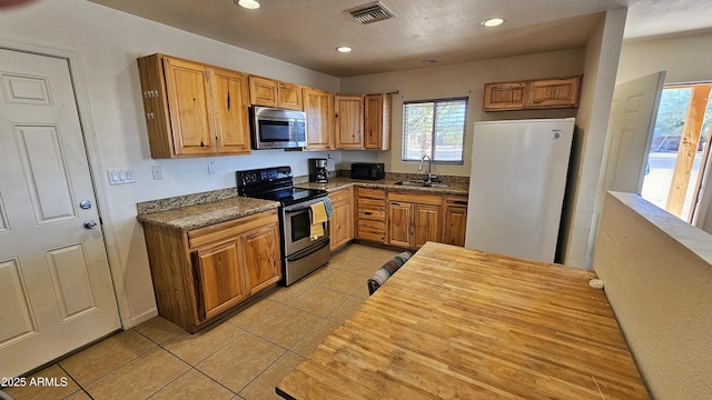 kitchen with sink, light tile patterned floors, a textured ceiling, and appliances with stainless steel finishes