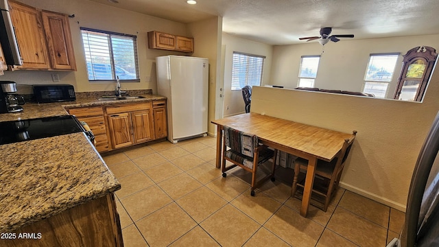 kitchen featuring white refrigerator, sink, light tile patterned floors, and dark stone counters