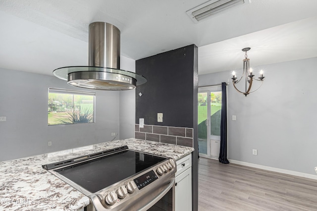 kitchen featuring stainless steel range with electric cooktop, island exhaust hood, light stone countertops, decorative backsplash, and white cabinets