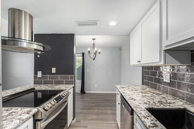 kitchen featuring wall chimney exhaust hood, light stone counters, appliances with stainless steel finishes, white cabinets, and backsplash