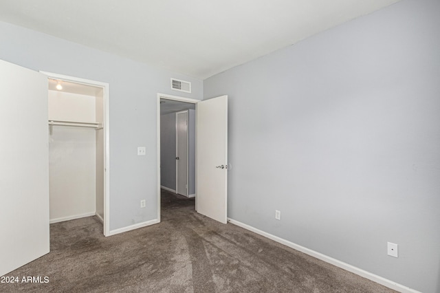 unfurnished bedroom featuring dark colored carpet, a walk in closet, and a closet