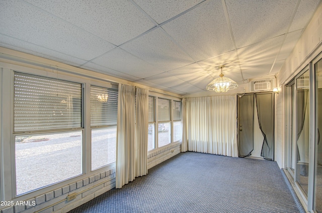 unfurnished sunroom with a drop ceiling, an inviting chandelier, and an AC wall unit