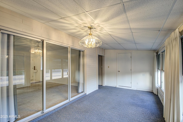 unfurnished sunroom featuring a notable chandelier and a drop ceiling