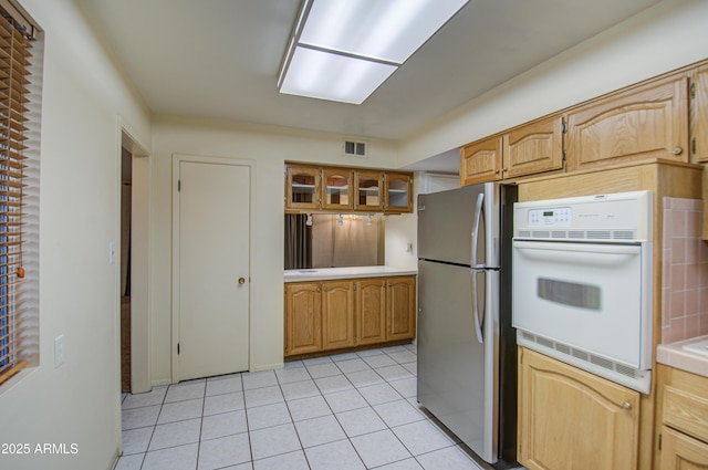 kitchen with freestanding refrigerator, tile countertops, white oven, glass insert cabinets, and light tile patterned floors