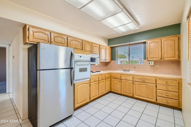 kitchen featuring light brown cabinets, a sink, backsplash, white appliances, and light tile patterned floors