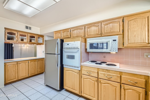 kitchen with visible vents, backsplash, white appliances, light tile patterned floors, and glass insert cabinets