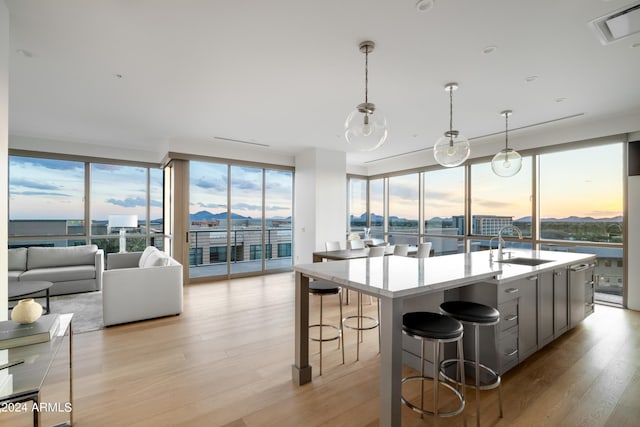 kitchen featuring light wood-type flooring, expansive windows, a spacious island, sink, and decorative light fixtures