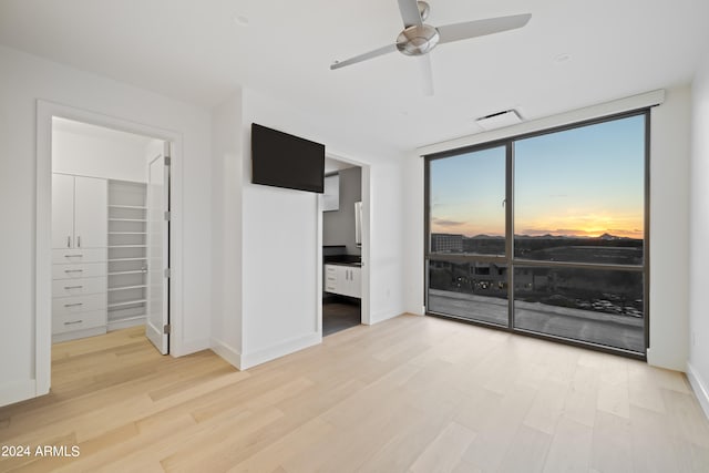 unfurnished bedroom featuring floor to ceiling windows, ensuite bathroom, light hardwood / wood-style flooring, ceiling fan, and a closet