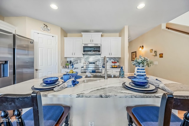 kitchen with stainless steel appliances, white cabinetry, sink, and a kitchen bar