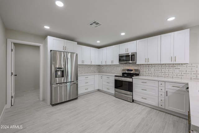 kitchen featuring appliances with stainless steel finishes, decorative backsplash, white cabinetry, and light hardwood / wood-style floors